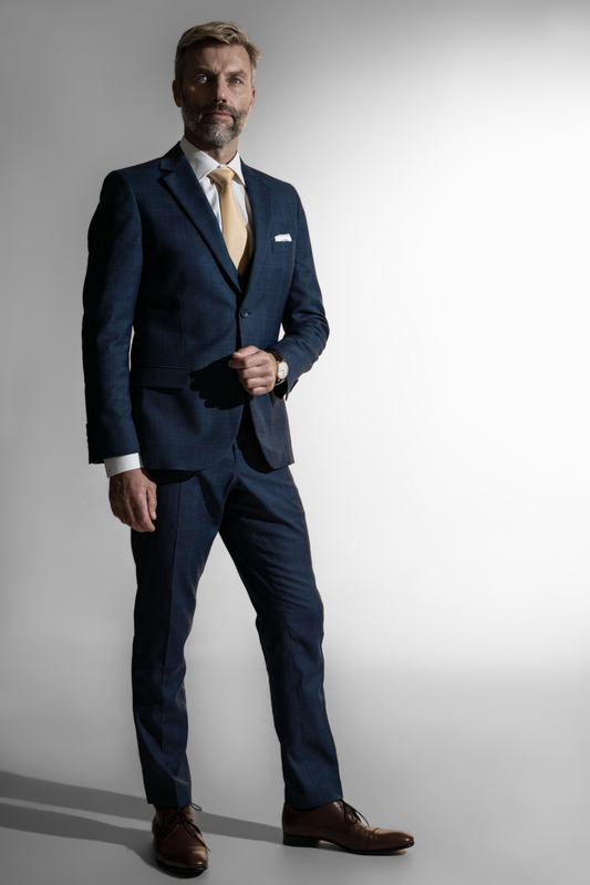 Elegant mand med gråt hår og skæg i en marineblå skræddersyet jakkesæk med en gul slips, poseret mod en neutral baggrund